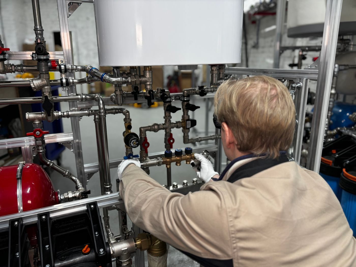 Engineer in white gloves working on boiler pipework and valves, seen from behind