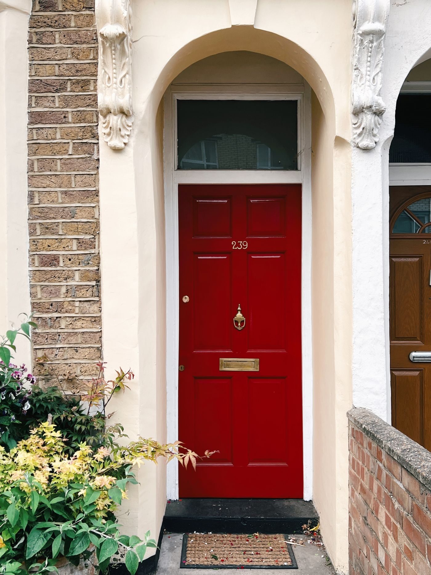 Red front door of a London townhouse with flowers by the step
